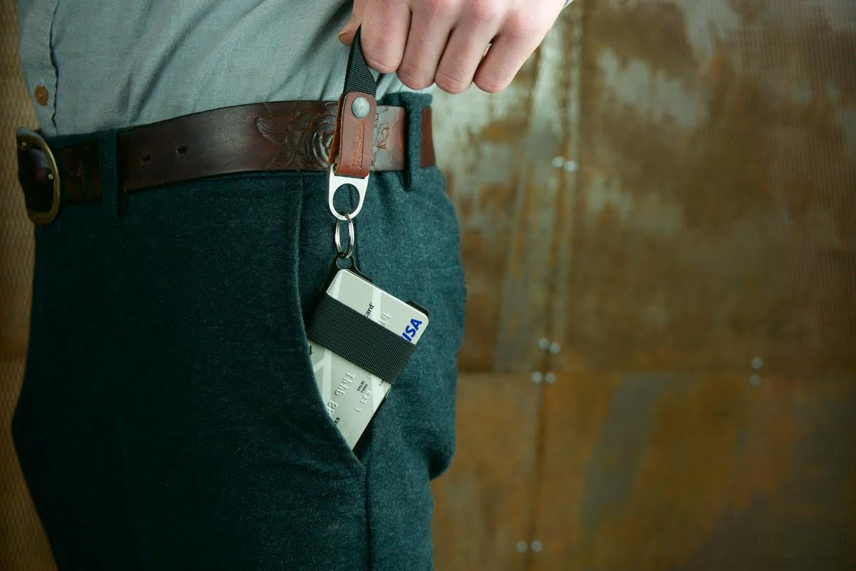 Armored summit wallet half way in pocket and connected to the keyton bottle opener keychain