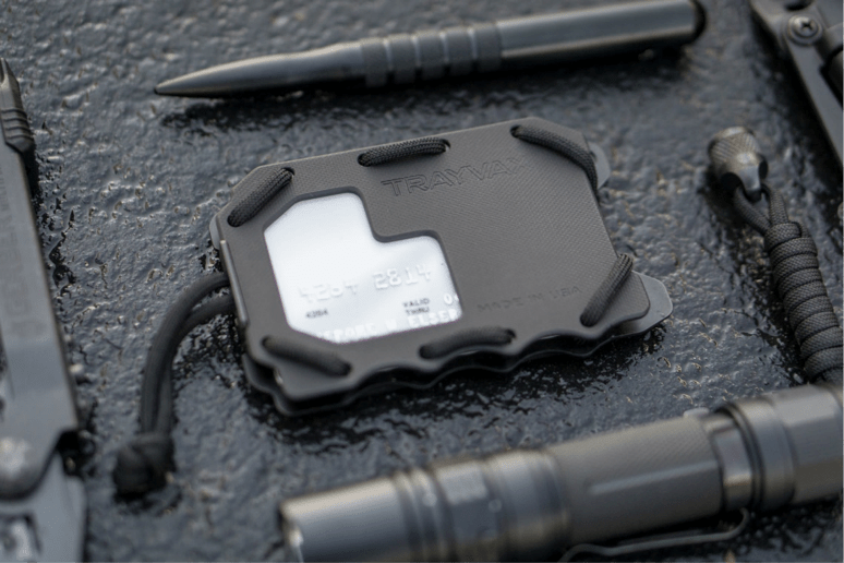 Black Trayvax Original 2.0 Wallet on black embossed material between a EDC pen and flashlight