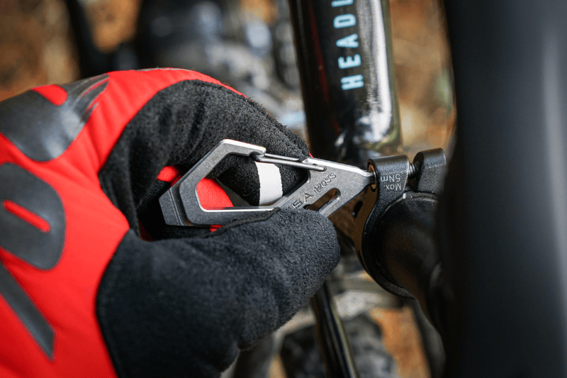Person wearing red and black gloves using a carabiner on a bicycle handlebar.